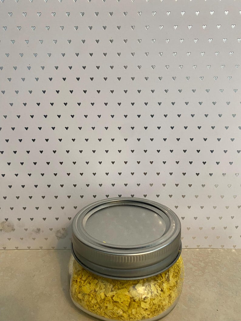 May include: A glass jar with a silver lid filled with yellow nutritional yeast flakes.