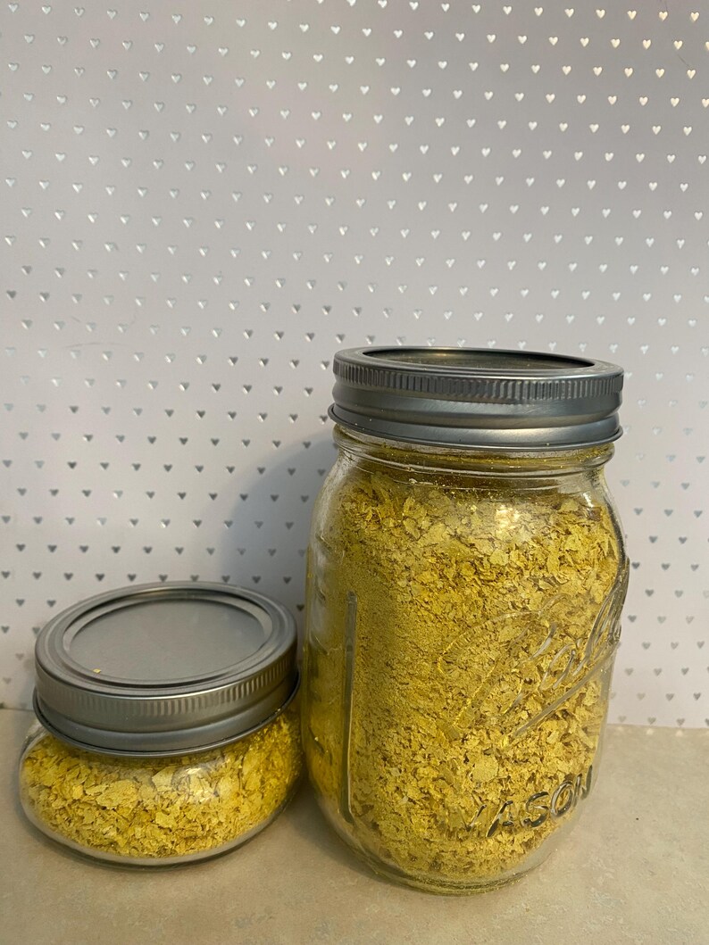 May include: Two glass jars filled with yellow nutritional yeast flakes. The jars have silver lids.