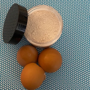 May include: A white powder in a clear jar with a black lid, next to three brown eggs on a blue and white patterned surface.