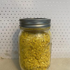 May include: A glass jar with a silver lid filled with yellow nutritional yeast flakes.
