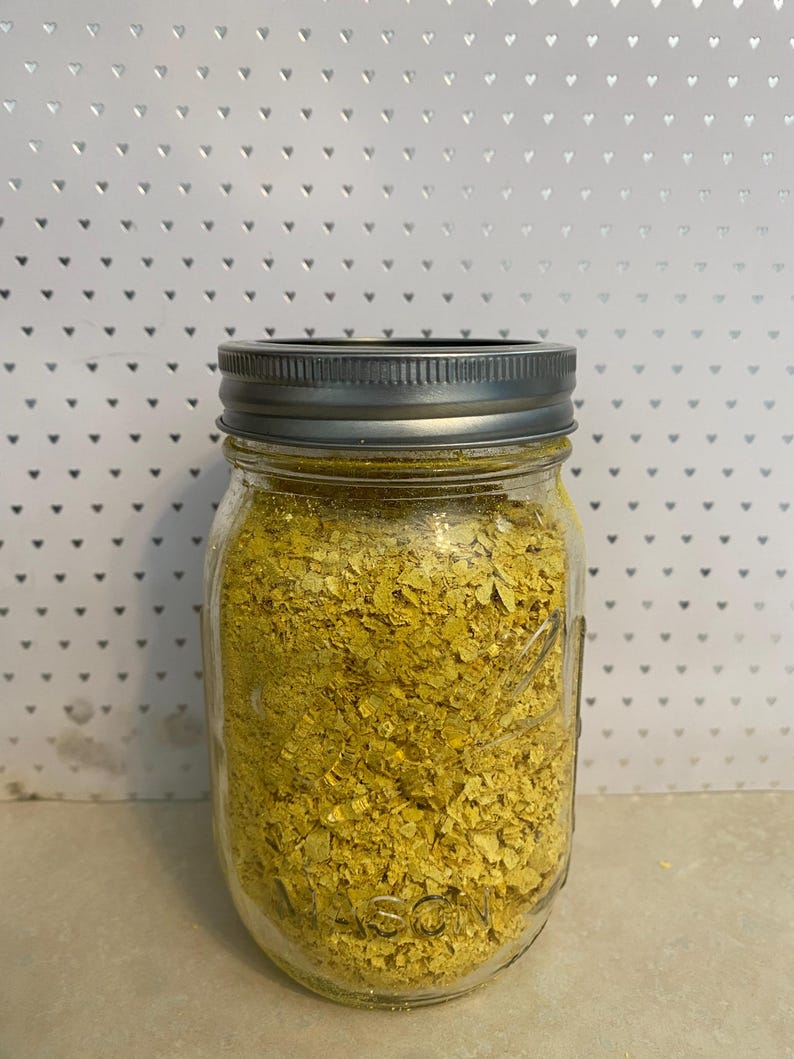 May include: A glass jar with a silver lid filled with yellow nutritional yeast flakes.