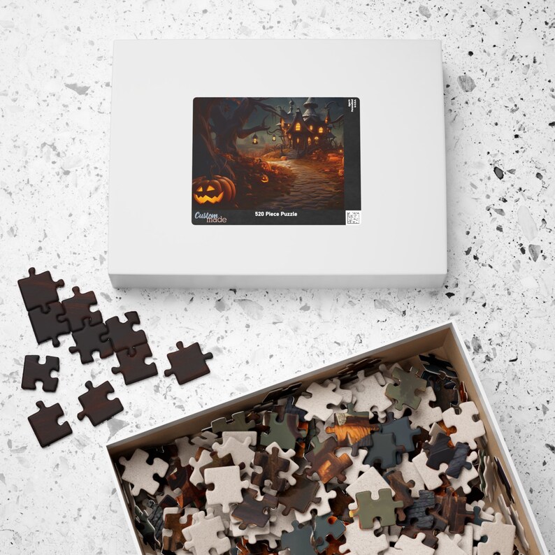 May include: A 520 piece jigsaw puzzle featuring a spooky Halloween scene with a haunted house, jack-o-lanterns, and a path leading to the house. The puzzle box is white with a picture of the puzzle on the front and the words "Custom Made" and "520 Piece Puzzle".
