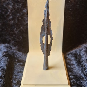May include: A bronze spearhead with a unique, jagged design. The spearhead is displayed on a cream-coloured stand.