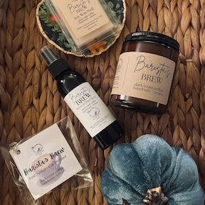 May include: A collection of coffee-scented products, including a soy wax melt, room and linen spray, car diffuser, and a jar candle. The products are labeled "Barista's Brew" with "dark roast coffee hazelnuts - cream" as the scent. A blue velvet pumpkin is also included.
