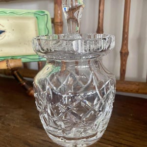 May include: A white ceramic mug with a black handle and the text "But First, Coffee" in a bold, black font. The mug is set against a blurred background, suggesting a cozy setting.