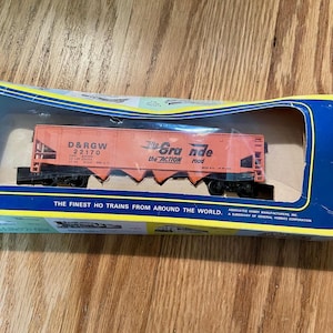 May include: An orange D&RGW 22170 model train car in its original packaging. The words "Rio Grande the ACTION road" are printed on the side. The packaging reads "THE FINEST HO TRAINS FROM AROUND THE WORLD."