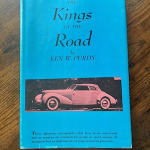 May include: A vintage book titled "The Kings of the Road" by Ken W. Purdy. The cover is a vibrant teal color, featuring a black and white image of a classic car. The book's text describes the automobiles as instruments of pleasure.
