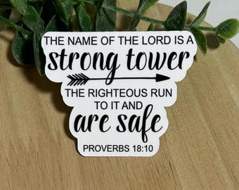 Può includere: Un adesivo bianco con testo nero. Il testo recita "THE NAME OF THE LORD IS A strong tower" con una grafica a freccia. Sotto, c'è scritto "THE RIGHTEOUS RUN TO IT AND are safe" e "PROVERBS 18:10". L'adesivo è su una superficie di legno.
