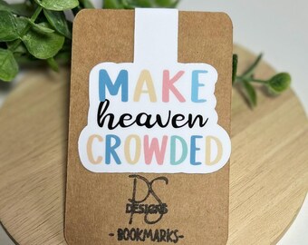 Może przedstawiać: Zakładka do książki z napisem "MAKE heaven CROWDED" w kolorowych literach. Zakładka znajduje się na brązowej karcie z logo "DS DESIGNS - BOOKMARKS-". Tło to drewniana powierzchnia z zielonymi liśćmi.
