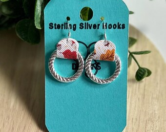 Może przedstawiać: Para srebrnych kolczyków koła z białym i pomarańczowym wzorem kwiatowym. Kolczyki znajdują się na turkusowej kartce z tekstem "Sterling Silver Hooks".