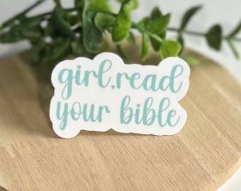 Może przedstawiać: Biała naklejka z napisem "girl read your bible" w jasnoniebieskiej czcionce. Naklejka znajduje się na drewnianej powierzchni, z zielonymi listkami w tle.