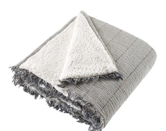 May include: A gray and white reversible throw blanket with a textured weave and fringe trim. One side is a soft, plush sherpa fabric, while the other side is a woven plaid pattern.