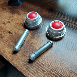 May include: Two silver metal cylinders with a red button on top. The buttons are round and have a silver rim.
