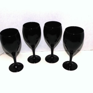 May include: Four black wine glasses with a classic stem design. The glasses have a glossy finish and are arranged on a white surface. The wine glasses are empty and ready to be filled.