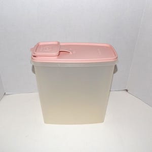 May include: A rectangular, translucent plastic container with a light pink lid. The lid has a smaller, attached pink section that can be opened and closed. The container is designed for food storage.