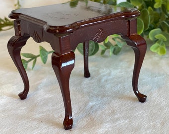 May include: A dark brown wooden table with four cabriole legs. The table has a square top and a smooth, polished finish.