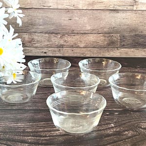 May include: A set of five clear glass bowls with a scalloped rim and horizontal ribbed detailing along the sides. The bowls are arranged in a cluster, each featuring a transparent finish and a circular base, showcasing a simple and functional design.