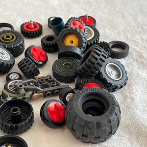 May include: A collection of various black toy tires, wheels, and related components. Some wheels have red or yellow centers. A small toy motorcycle is also present. The tires vary in size and tread pattern.