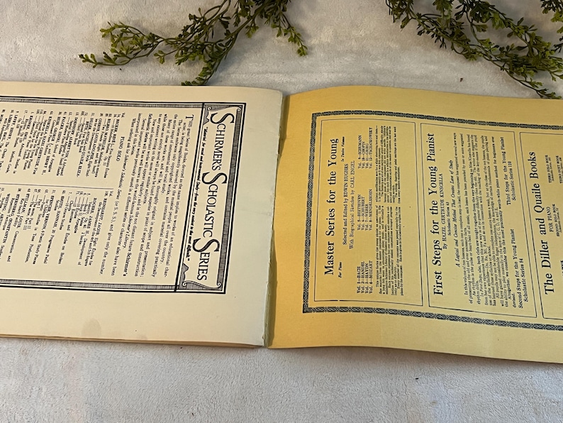 May include: Open vintage book pages with text, featuring "SCHIRMER'S SCHOLASTIC SERIES" and "Master Series for the Young." The pages are cream-colored with black text and borders. Greenery is visible in the background.