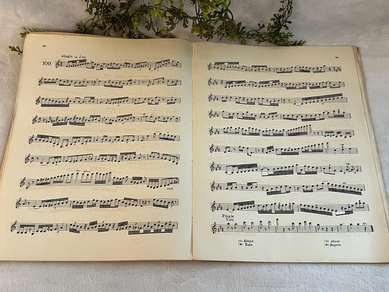 May include: Open vintage sheet music book with two pages of musical notation. The pages are aged with a cream color, and the musical notes are printed in black ink. The text "Adagio" and "Finale" are visible.