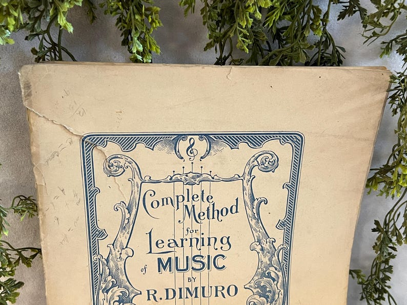 May include: An antique book cover with the title "Complete Method for Learning Music" in blue script. The cover has an ornate blue border and is set against a beige background. The book is slightly worn.