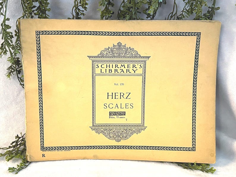 May include: A vintage book cover with the text "Schirmer's Library" and "Herz Scales." The cover is a light yellow color with a black decorative border and text. The book is slightly worn, suggesting it is an antique.
