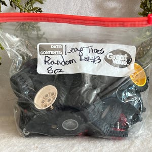 May include: A clear plastic bag with a red zipper contains a random assortment of black Lego tires. A white label reads "Lego Tires, Random Lot #3, 8oz". Some tires have tan or yellow accents.