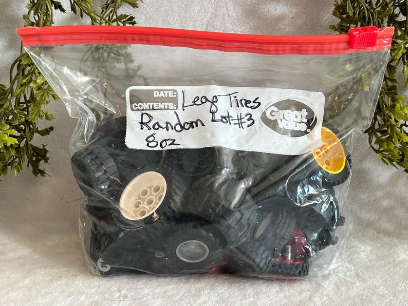 May include: A clear plastic bag with a red zipper contains a random assortment of black Lego tires. A white label reads "Lego Tires, Random Lot #3, 8oz". Some tires have tan or yellow accents.