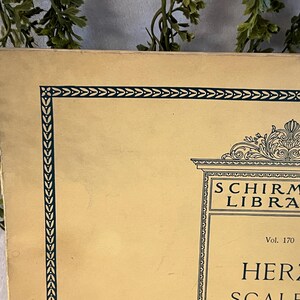 May include: A vintage book cover with a cream-colored background and a dark green border. The text "SCHIRMER'S LIBRARY" is visible, along with "HERZ SCALES". The cover has an ornate design at the top and is slightly worn.