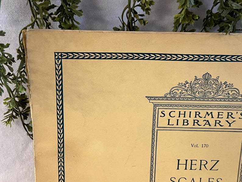 May include: A vintage book cover with a cream-colored background and a dark green border. The text "SCHIRMER'S LIBRARY" is visible, along with "HERZ SCALES". The cover has an ornate design at the top and is slightly worn.