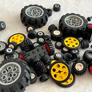 Op de afbeelding: Een verzameling zwarte, grijze en gele speelgoedwielen en bijbehorende onderdelen, waaronder banden, assen en naven. De wielen vari&euml;ren in grootte en ontwerp, sommige hebben gele centra en andere witte of grijze details. De onderdelen zijn verspreid over een wit oppervlak.