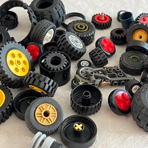 May include: A collection of black toy wheels of various sizes, some with yellow, red, or gold centers. The tires have textured treads. There are also other toy parts in the image.