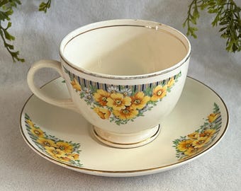 Taza y platillo vintage de Cunningham & Pickett decorados a mano con flores amarillas, rayas azules y estampado de nautilus y acacia color blanco hueso. DESCONCHADOS.
