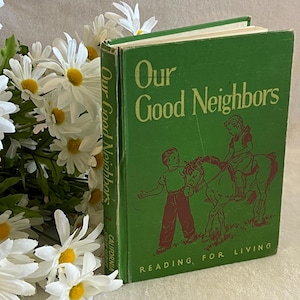 May include: A vintage green book titled "Our Good Neighbors" with illustrations of children and a horse. The book is part of the "Reading for Living" series. White daisies are in the background.