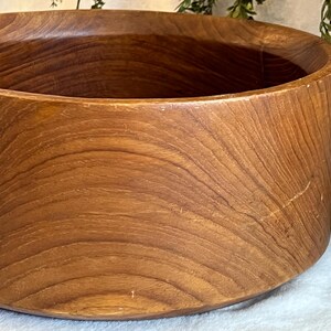 May include: A large, round wooden bowl with a warm, brown finish. The bowl's exterior features a smooth, curved design with visible wood grain patterns. The bowl is suitable for serving salads or as a decorative piece.