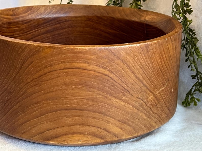 May include: A large, round wooden bowl with a warm, brown finish. The bowl's exterior features a smooth, curved design with visible wood grain patterns. The bowl is suitable for serving salads or as a decorative piece.