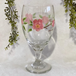 Könnte beinhalten: Ein klares Glasgefäß mit einem Blumendesign mit rosa Blüten und grünen Blättern. Das Gefäß hat einen Stiel und einen runden Boden. Das Wort "Franconia" ist auf der Seite des Gefäßes aufgedruckt.