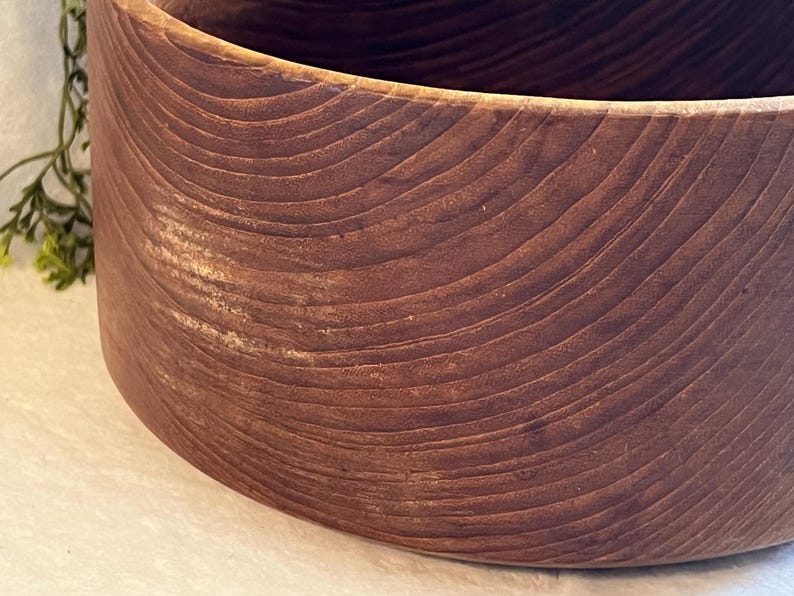 May include: A close-up of a large, round wooden bowl. The bowl is made of dark brown wood with visible grain patterns. The bowl's exterior has a smooth, curved surface.