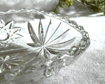 May include: Clear glass serving dish with starburst and floral etched designs. The rim has a scalloped edge. The dish is oval-shaped and sits on a white surface.