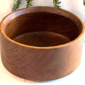 May include: A round, wooden bowl with a rich, brown color. The bowl has a smooth, polished interior and exterior, showcasing the natural wood grain. The bowl's design is simple and classic, suitable for various uses.