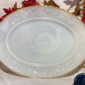 Puede incluir: Plato ovalado blanco con borde dorado y diseño de pavo en relieve en el centro. El plato tiene un borde decorativo con motivos florales y frutales en relieve. Una pieza festiva para Acción de Gracias u otras ocasiones especiales.