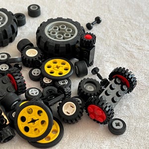 Op de afbeelding: Een verzameling zwarte en gele speelgoedautowielen en banden, met verschillende maten en ontwerpen. Sommige wielen hebben gele centra, andere witte of grijze. De banden hebben een getextureerd, off-road profiel.