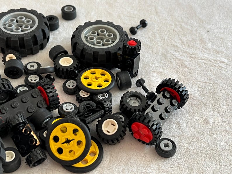 Op de afbeelding: Een verzameling zwarte en gele speelgoedautowielen en banden, met verschillende maten en ontwerpen. Sommige wielen hebben gele centra, andere witte of grijze. De banden hebben een getextureerd, off-road profiel.