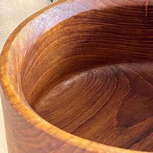 May include: Close-up of a handcrafted wooden bowl. The bowl is made of a rich, dark brown wood with visible grain patterns. The interior and exterior surfaces are smooth, showcasing the natural wood tones and textures. The bowl's shape is round with a wide opening.