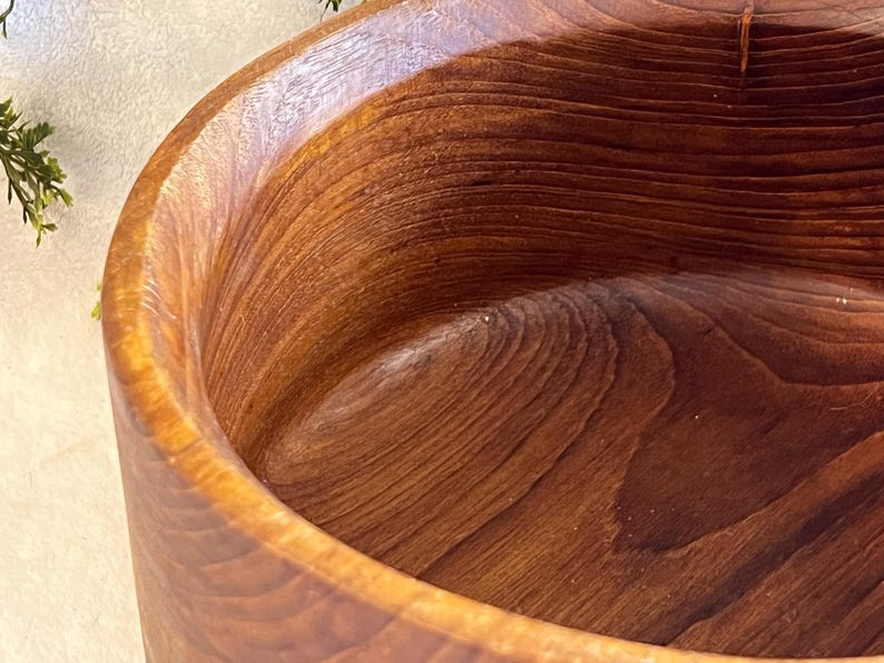 May include: Close-up of a handcrafted wooden bowl. The bowl is made of a rich, dark brown wood with visible grain patterns. The interior and exterior surfaces are smooth, showcasing the natural wood tones and textures. The bowl's shape is round with a wide opening.