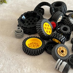 May include: A collection of black toy wheels with yellow and gold centers. Various sizes and styles of wheels are scattered across a light-colored surface, including some with red accents. The image showcases a variety of toy vehicle components.