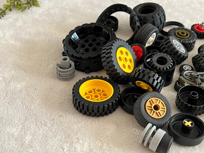 May include: A collection of black toy wheels with yellow and gold centers. Various sizes and styles of wheels are scattered across a light-colored surface, including some with red accents. The image showcases a variety of toy vehicle components.