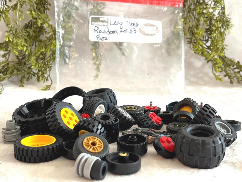 May include: A collection of black Lego tires with yellow, red, and white accents. The tires vary in size and tread pattern. A plastic bag in the background has the text "Leaf Tires Random Lot #3 8oz."