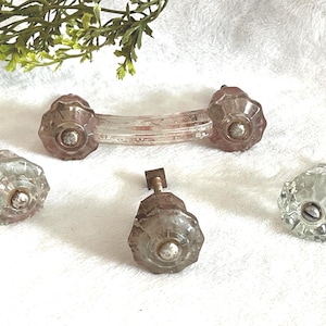 May include: A collection of vintage glass cabinet knobs and a matching pull. The knobs are clear with a faceted design and metal hardware. The pull is curved and has a similar design. The hardware is a tarnished silver color.