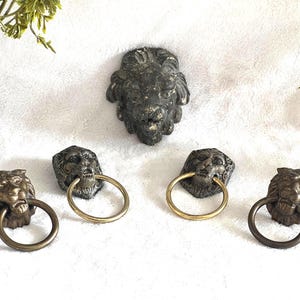 May include: A selection of antique lion head drawer pulls and a larger lion head wall mount. The drawer pulls feature brass rings and are in bronze tones. The wall mount is a darker, weathered bronze finish.